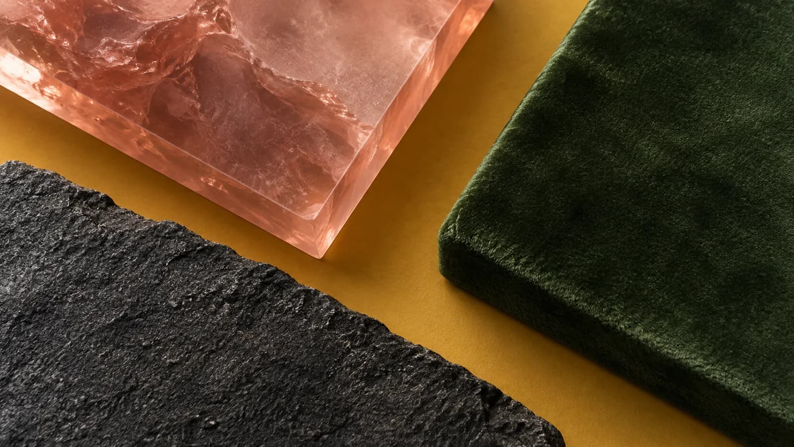 Rose resin, moss-green velvet and rough basalt layered on a muted mustard ground