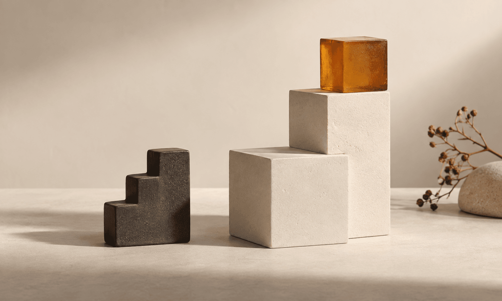 A small stepped charcoal shape stands beside larger ivory blocks and an amber cube