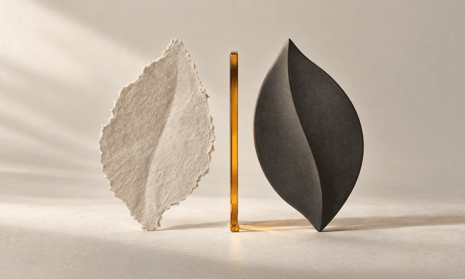 A torn, rough-edged ivory paper leaf beside the same leaf shape cut cleanly from charcoal ceramic, with an amber line between them