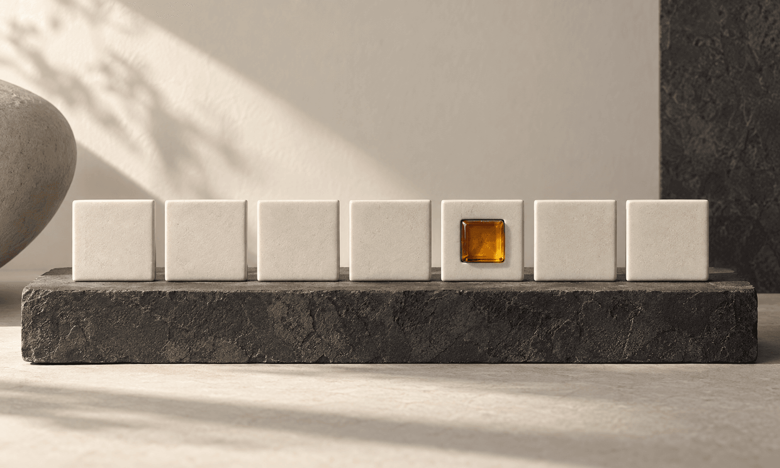 A row of seven identical ivory ceramic tiles on a charcoal slab, the fifth with a small amber glass inset