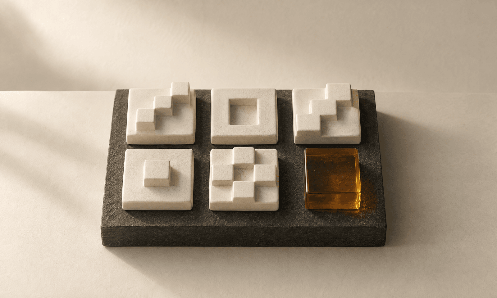 Six small ivory ceramic tiles carved with stepped relief on a charcoal slab, with one amber glass cube among them
