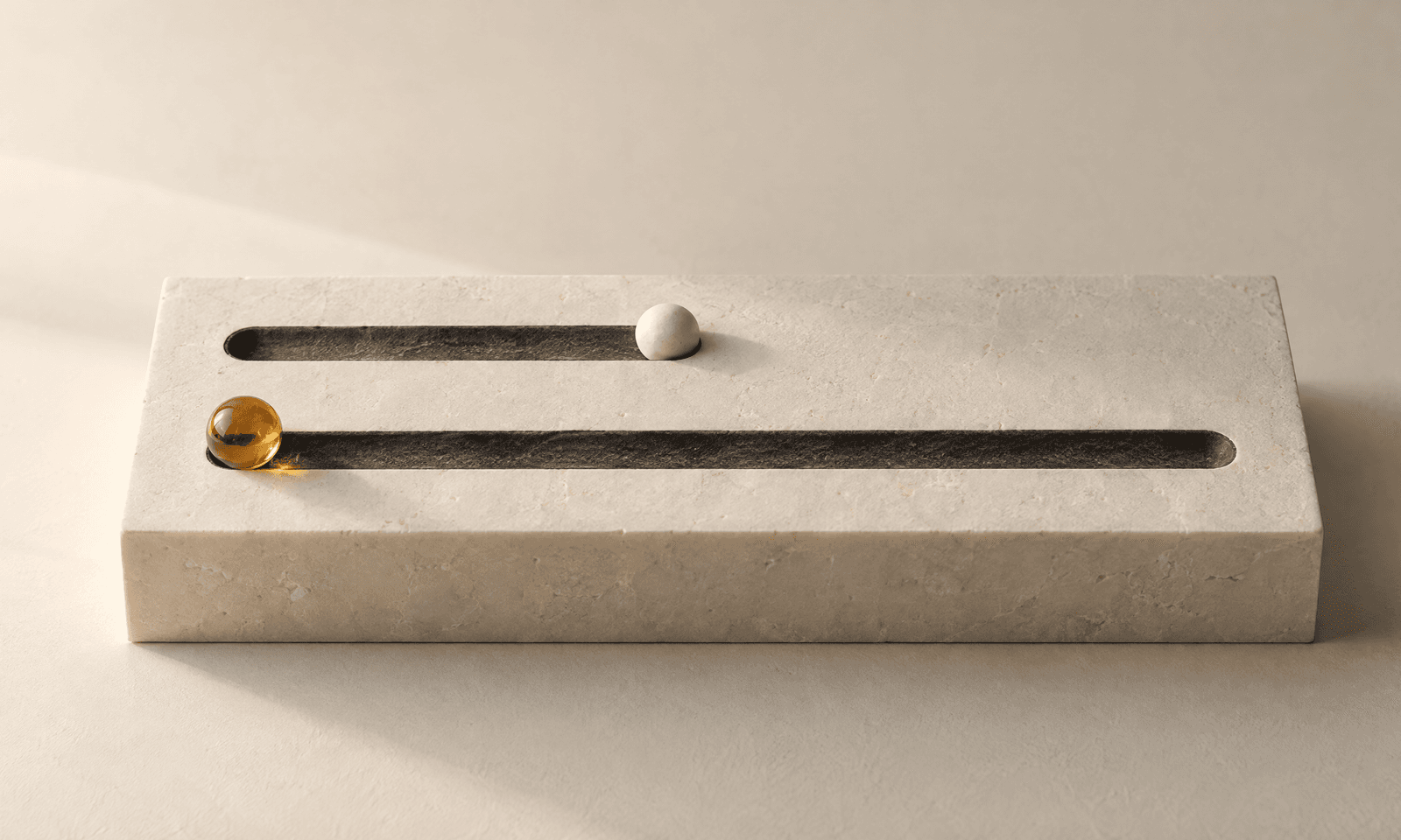 A pale stone slab with one short and one long channel cut into it, a small ceramic ball at the end of the short channel and an amber glass ball at the start of the long one