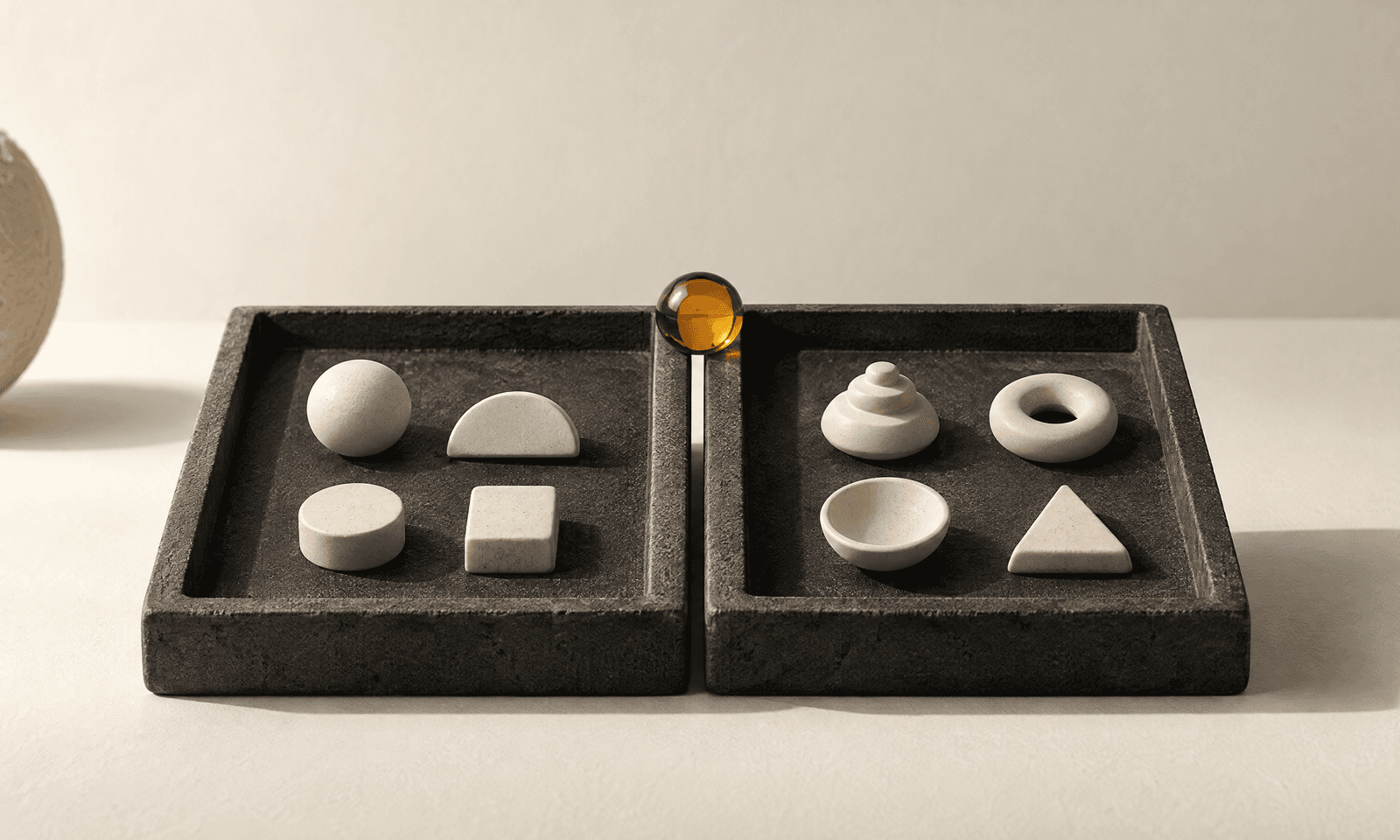 Two shallow dark trays side by side holding pale ceramic tokens sorted between them, with one amber glass token resting on the divider