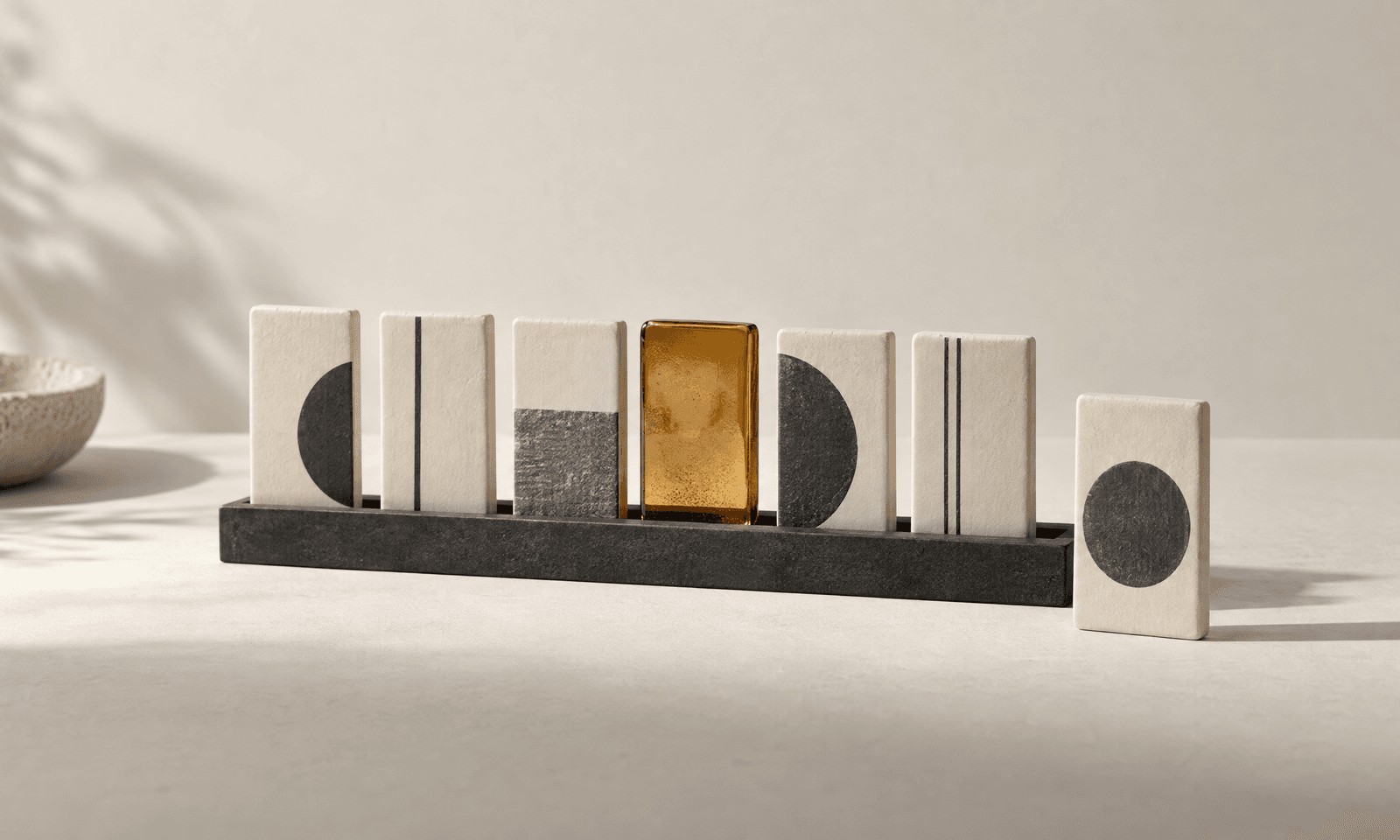 Seven pale upright tiles standing in a slim dark rail with one tile turned to face forward and one amber glass tile among them