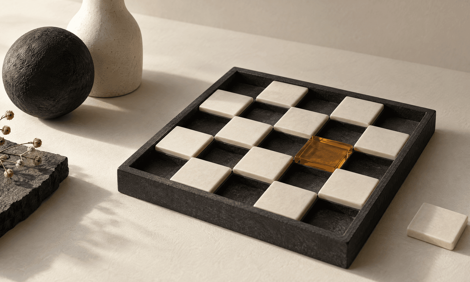 A dark stone tray holding pale ceramic tiles in a checkerboard, with several bays empty and one amber glass tile among them