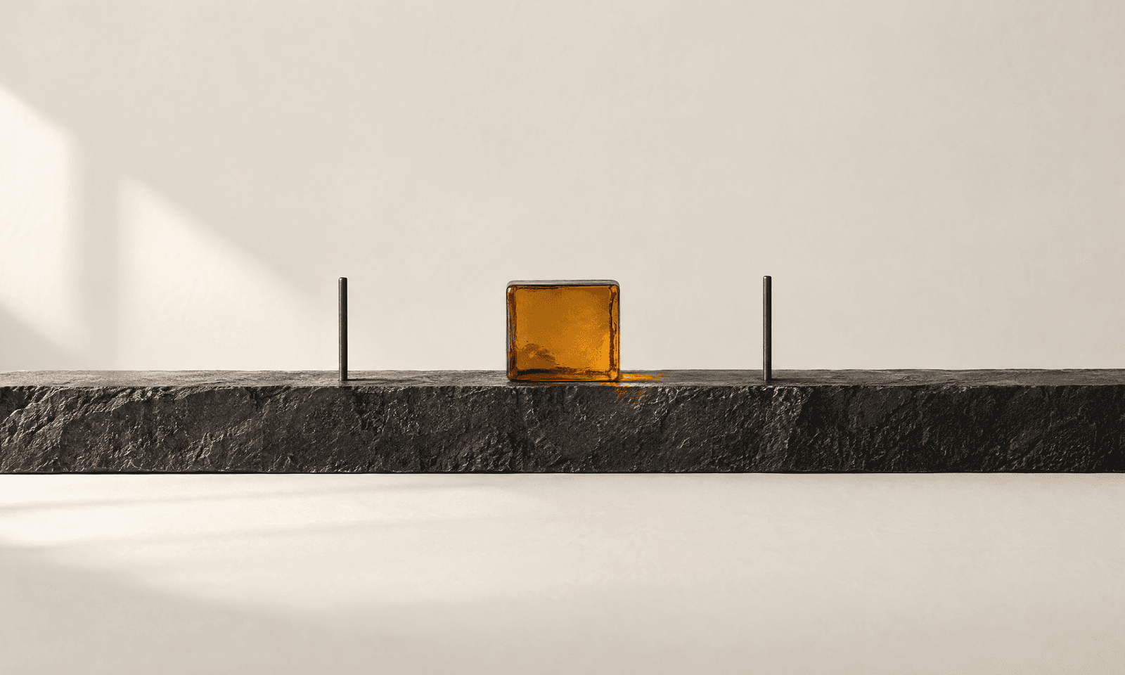 A long dark stone band running across a pale surface with a small amber glass square at its centre and two slim rods marking narrower limits