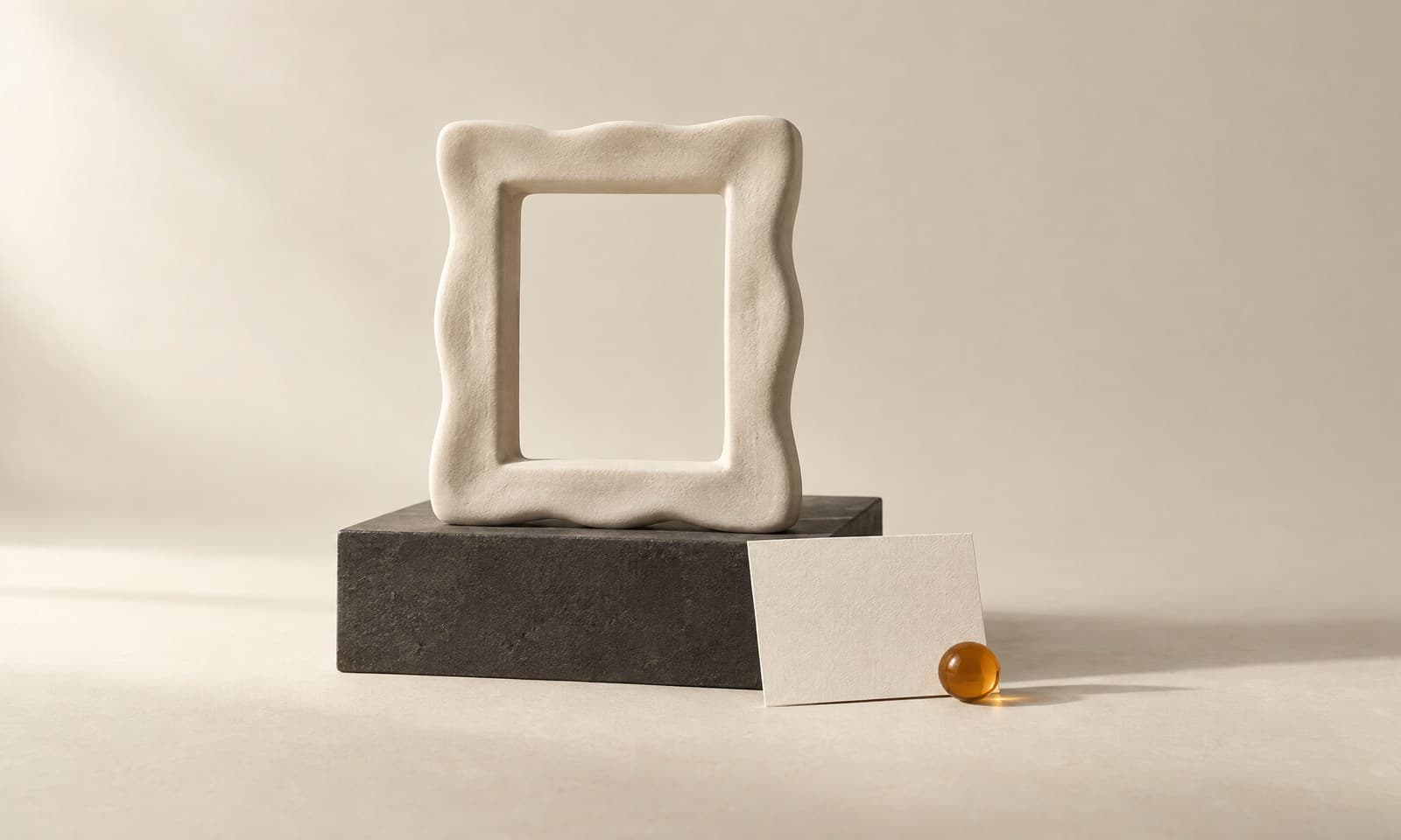An empty ivory ceramic picture frame on a charcoal plinth with a small blank paper label leaning against it and an amber glass bead on the label