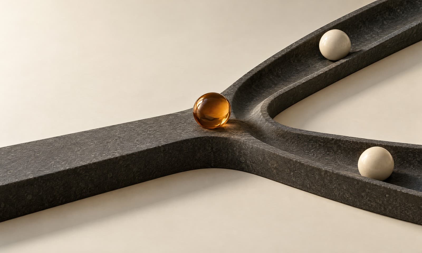 A charcoal ramp forking into two channels with ivory ceramic balls in each and an amber ball poised at the fork