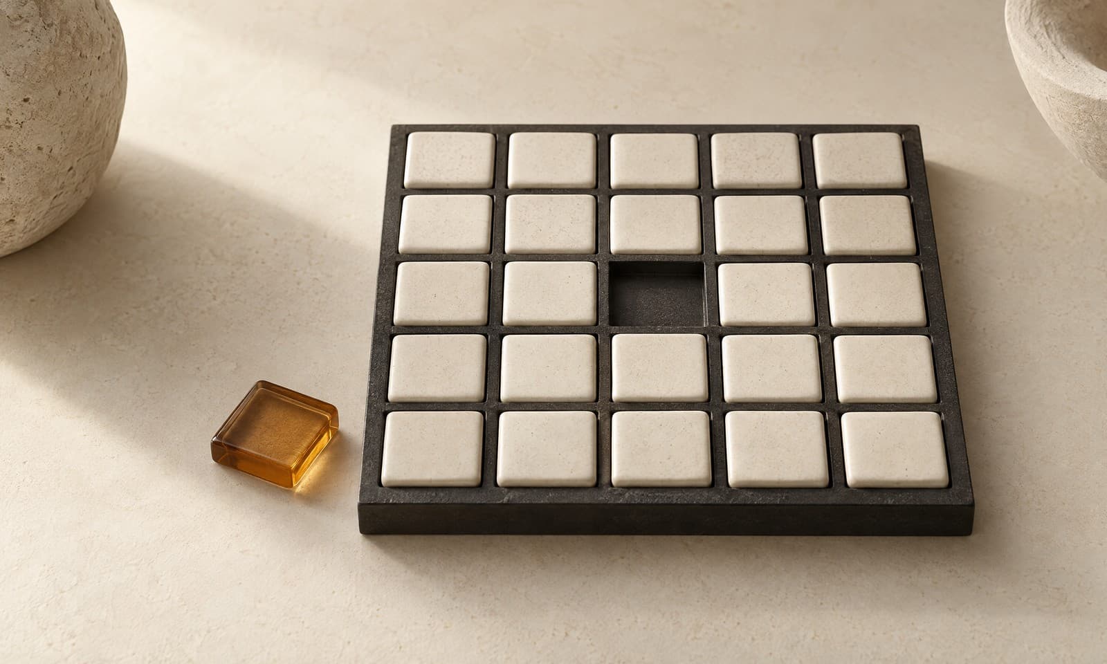 A charcoal grid frame holding ivory ceramic tiles in every slot but one, with an amber tile lying outside the frame