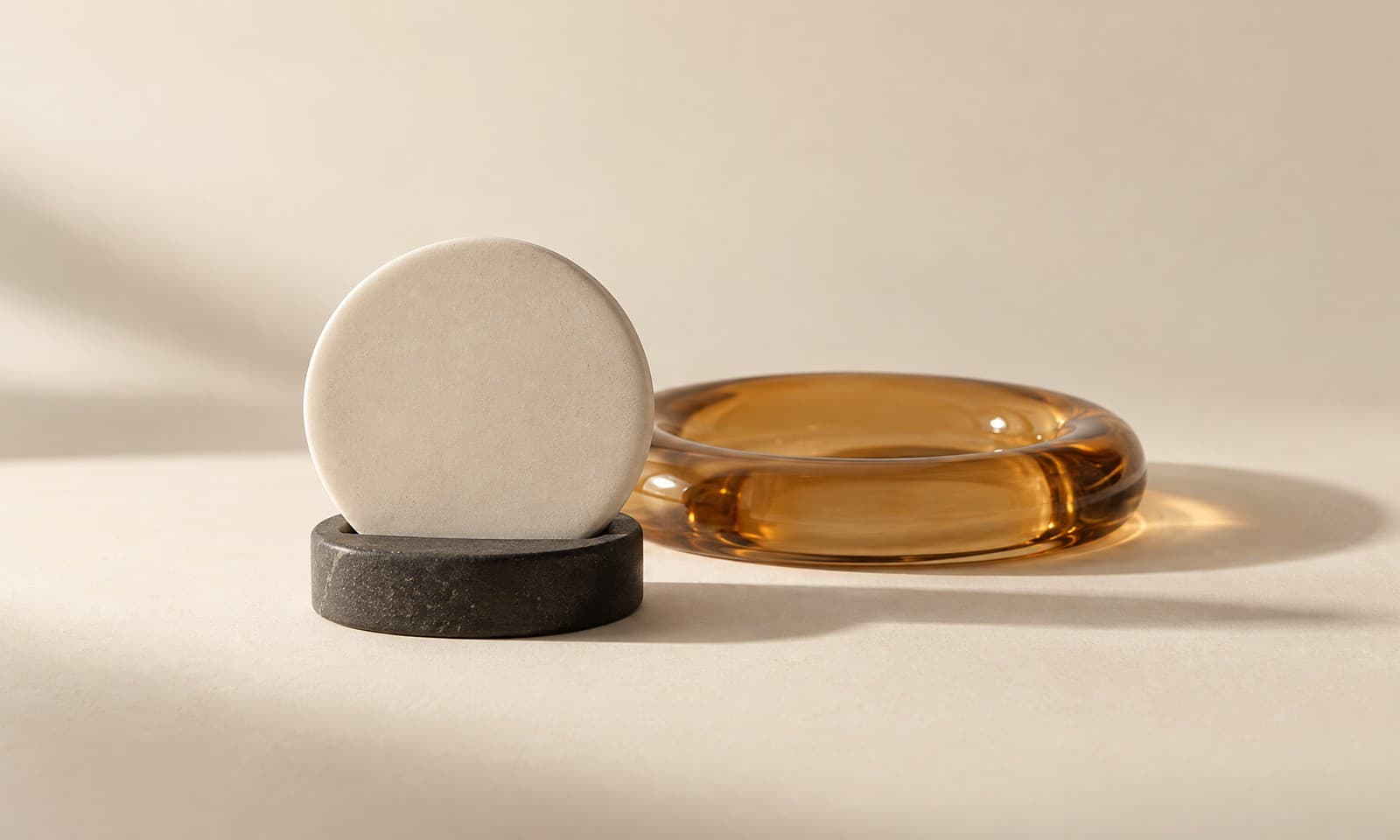 A small round ivory ceramic disc standing in a slim charcoal ring holder with an amber glass ring behind it