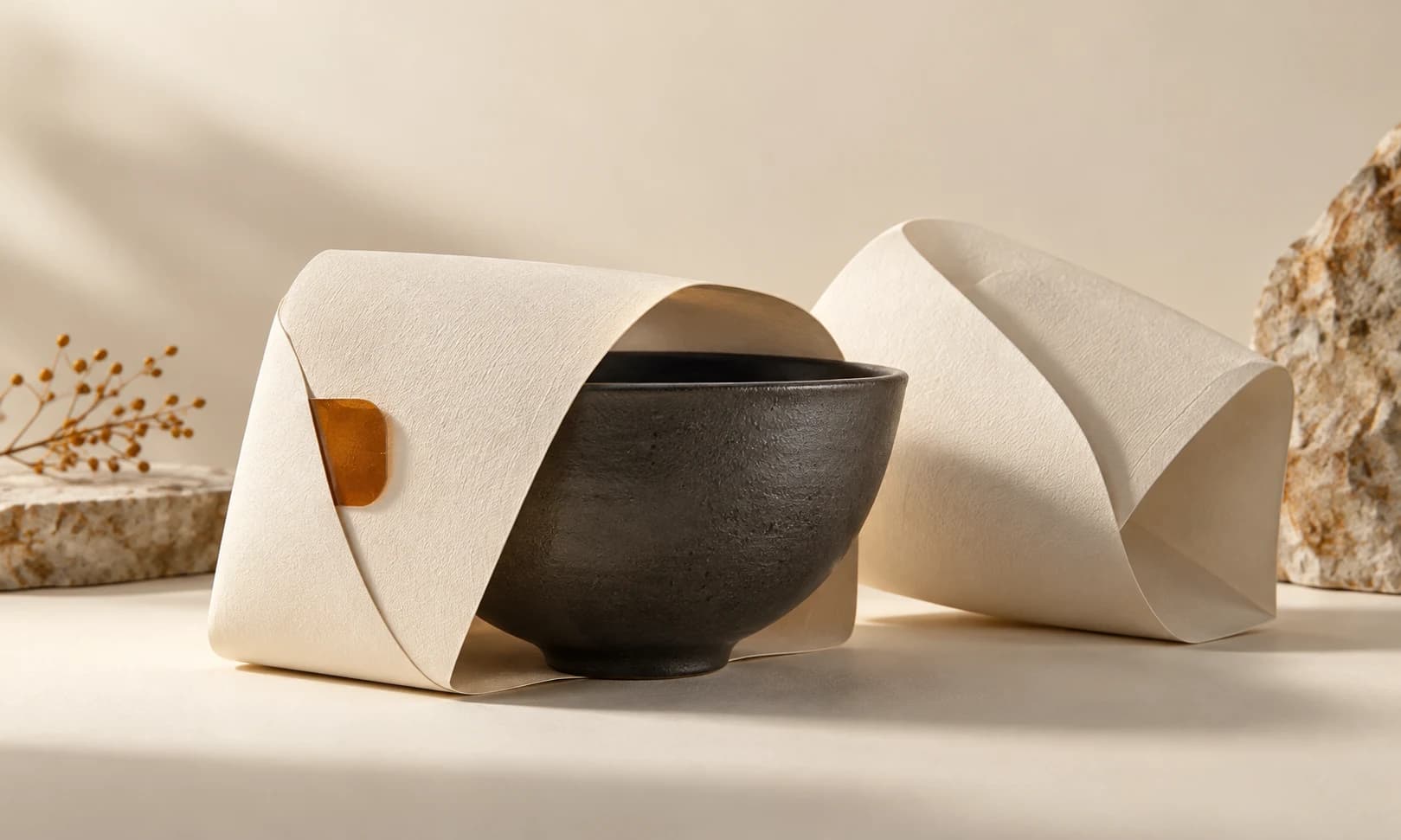 Ivory paper sleeves around a charcoal ceramic bowl with a small amber tab